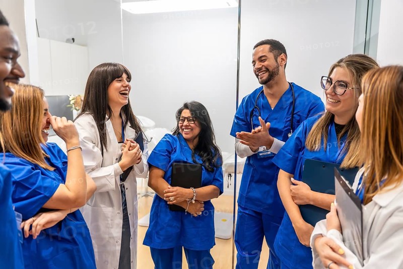 Diverse medical professionals wearing scrubs and lab coats interacting happily and laughing together in a healthcare setting, brainstorming ideas while sharing a moment of camaraderie and teamwork