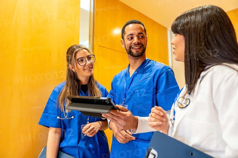 Medical team of diverse healthcare workers standing together, reviewing patient data or health records on a digital tablet, fostering teamwork and modern communication in a hospital setting