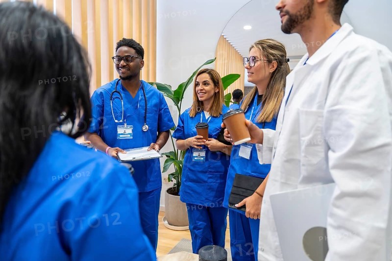 Diverse medical professionals wearing scrubs and lab coats collaborating, discussing patient care, and teamwork during a professional meeting in a modern medical facility