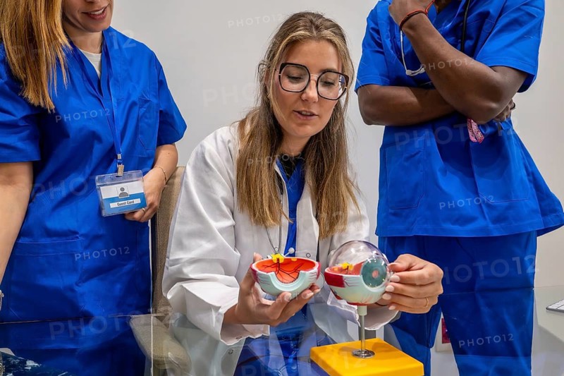 Medical professional instructing students, explaining human eye anatomy with a detailed model in a classroom or hospital setting, supporting medical education and practical learning