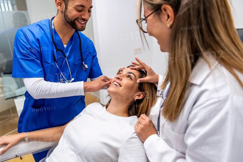 Medical team consisting of a doctor and a nurse examining a young female patient's face in a modern clinic, focusing on cosmetic dermatology and aesthetics