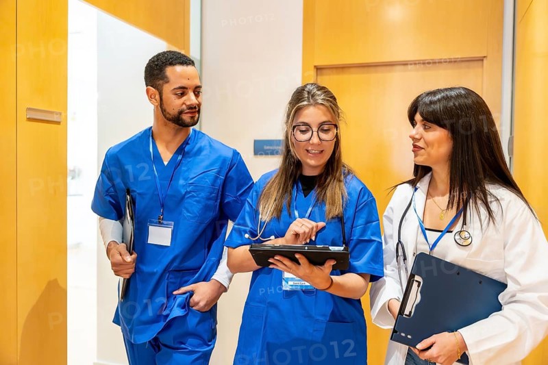 Healthcare professionals walk down a hospital corridor, consulting a digital tablet and clipboard as doctors and nurses collaborate on patient information and treatment plans