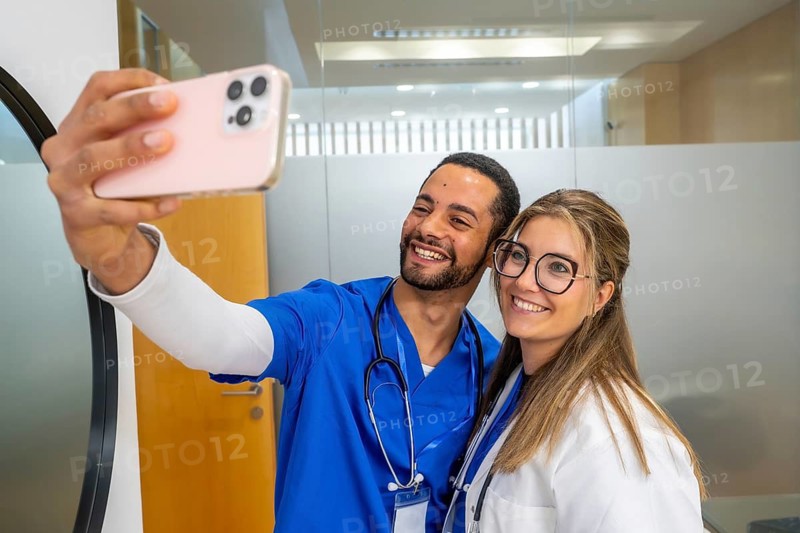 Two smiling healthcare professionals male in scrubs and female in lab coat and glasses take a cheerful selfie with a smartphone, conveying teamwork, success and modern medical collaboration