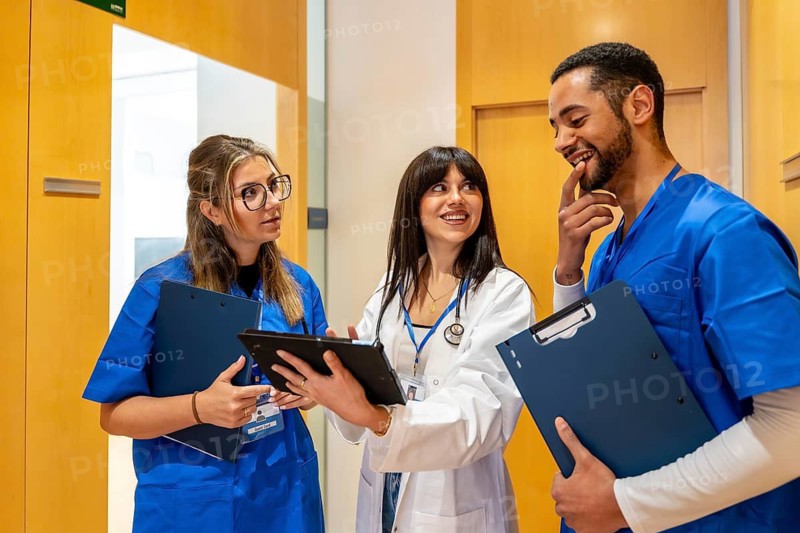 Diverse medical team of doctors and nurses consulting over a tablet and clipboards in a hospital corridor, collaborating on patient care with focus, technology and professionalism