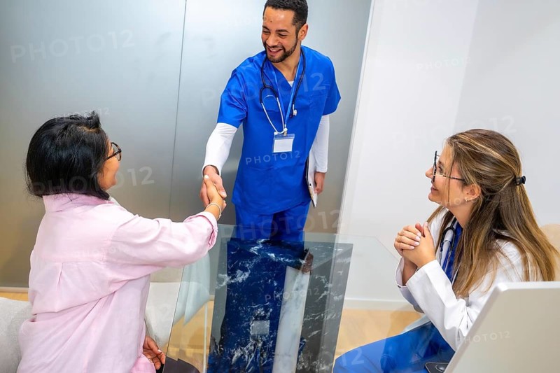 Medical professional in blue scrubs shaking hands with a woman patient, signifying trust and communication during a healthcare consultation with a doctor in a modern clinic