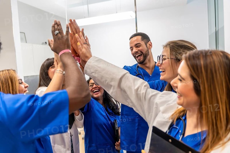 Diverse medical team of happy doctors and nurses stacking hands in a high five gesture, celebrating a successful outcome, showing unity, collaboration, and achievement in their healthcare profession