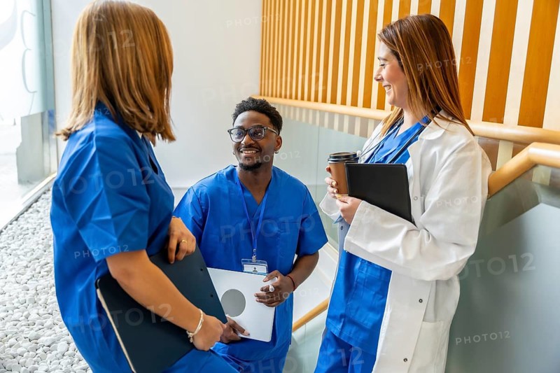 Diverse medical team members, including a doctor and nurses, engaging in a smiling, informal discussion during a break in a modern hospital or clinic setting