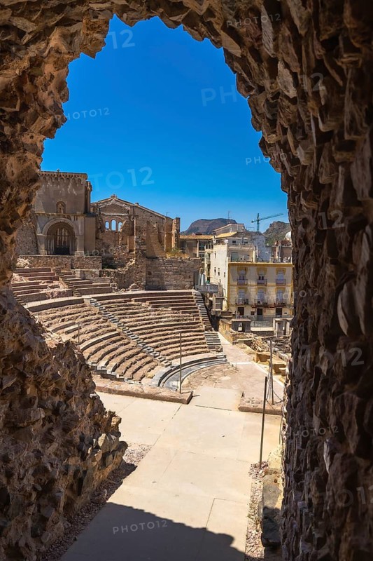 Roman theatre in cartagena, murcia, spain, showcasing ancient architecture, historical ruins, and tiered seating framed by a stone archway under a clear blue sky