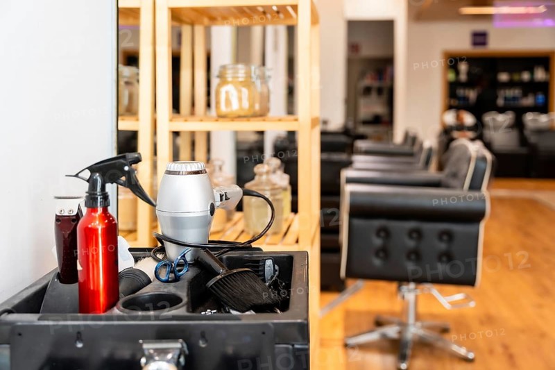 Styling tools and equipment arranged on a barber cart. Including a hair dryer and spray bottle. Defining the professional workspace of a hair salon or barbershop with customer chairs in the background