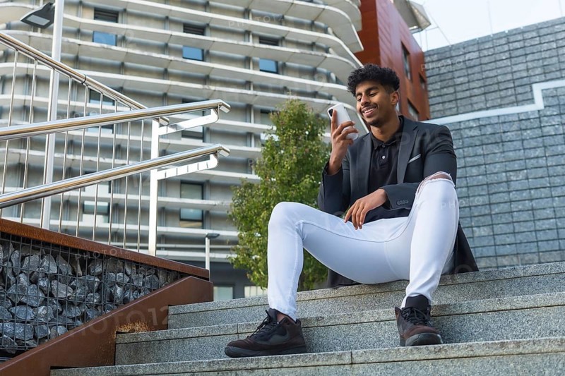 Low angle view of an Arab businessman sitting in outdoor stairs using phone