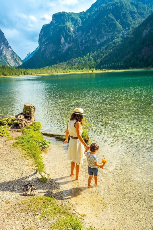 Mother and son wading in the crystal clear water of lake dobbiaco, surrounded by the breathtaking scenery of the dolomites, enjoying a peaceful summer vacation