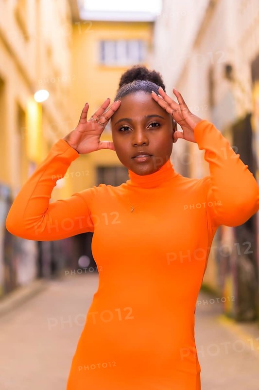 Fashionable urban style with a black African girl in an orange dress and black heels on a city street. Portrait looking at camera