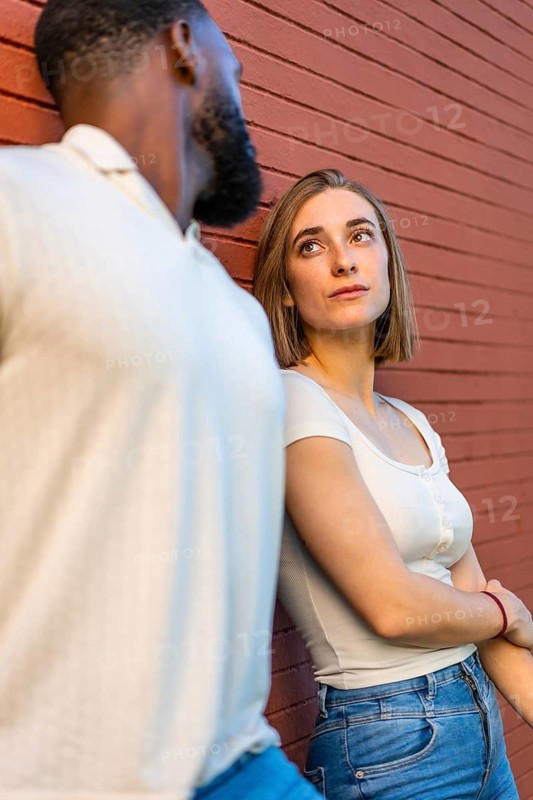 Vertical side view of a caucasian woman looking at her african partner leaning on wall