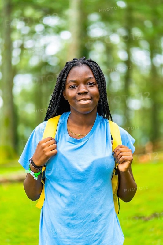 Vertical portrait of a joyful african female backpacker with braided hair enjoying adventure in natural parkland