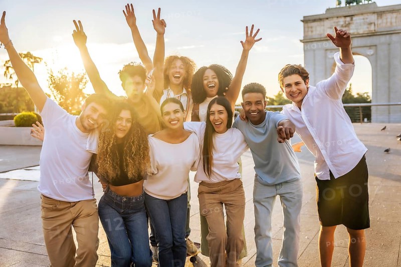 Formal portrait of a group of multi-ethnic friends raising arms enjoying together in the city during sunset