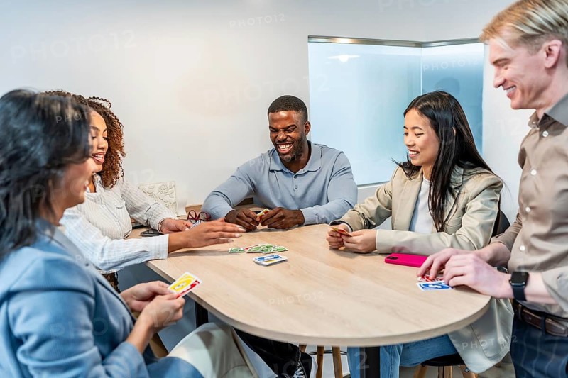 Happy multi ethnic coworkers playing cards at the office desk during a break, enjoying some leisure time together