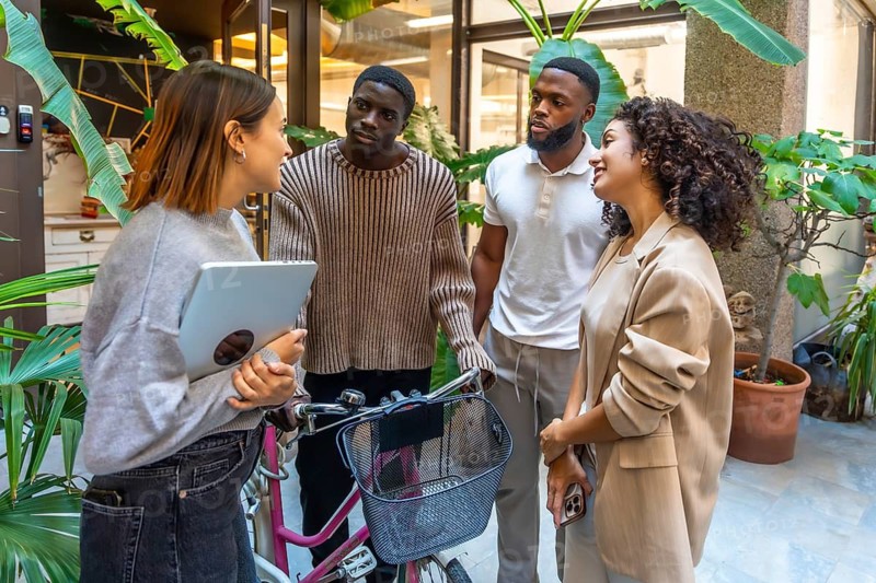 Diverse team of coworkers talking out the office building holding bike and laptop