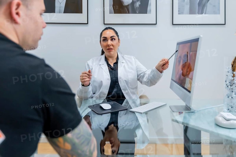Doctor in a lab coat is showing a patient images on a computer screen, explaining aesthetic procedure details during a consultation in a modern medical office