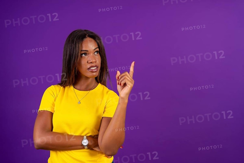 Studio portrait with purple background of a modern african woman looking up and pointing with finger