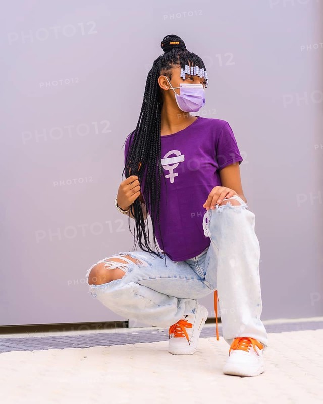 International women's day in the year of the coronavirus pandemic, covid-19. Dominican woman with feminist purple shirt and face mask, gray plain background