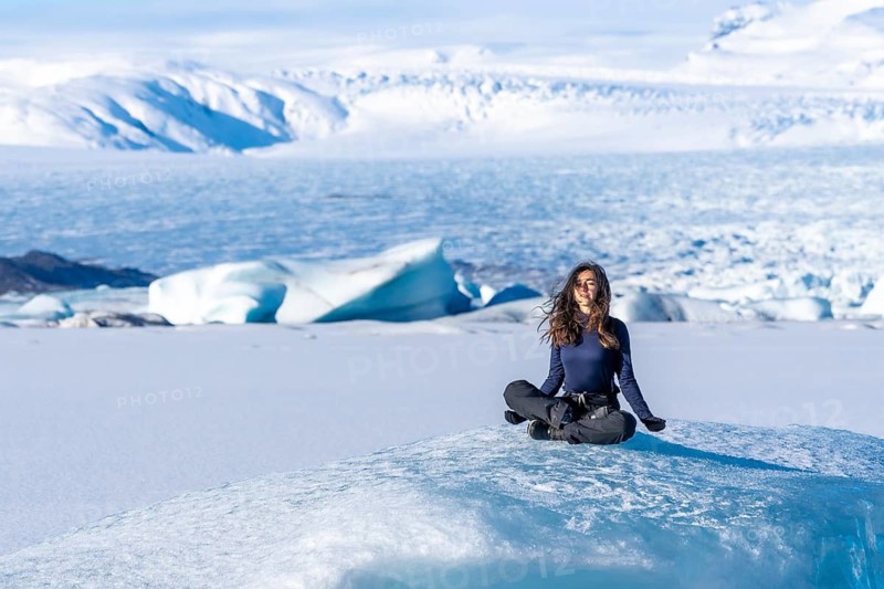 A woman is sitting on a block of ice in the snow. Concept of solitude and tranquility, as the woman is alone in the vast, snowy landscape. The stillness of the scene