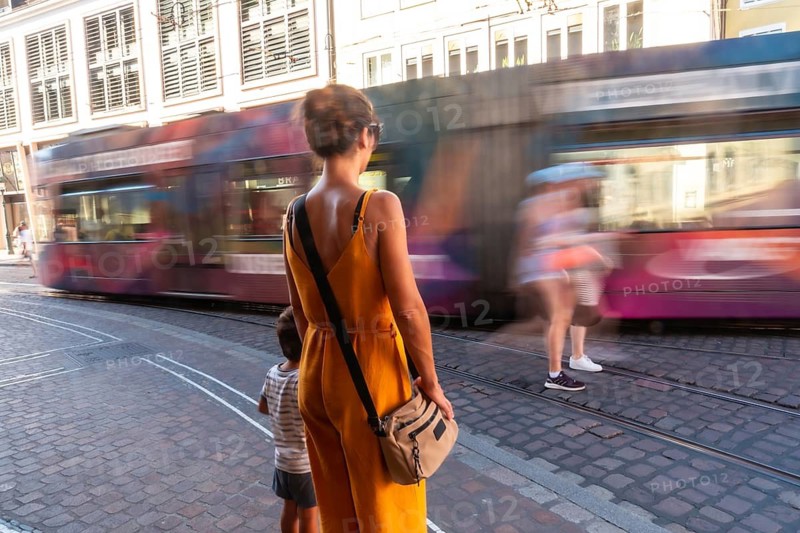A woman in a yellow dress is walking down a street with a child in a striped outfit. She is carrying a handbag and she is in a hurry. freiburg im breisgau, freiburg