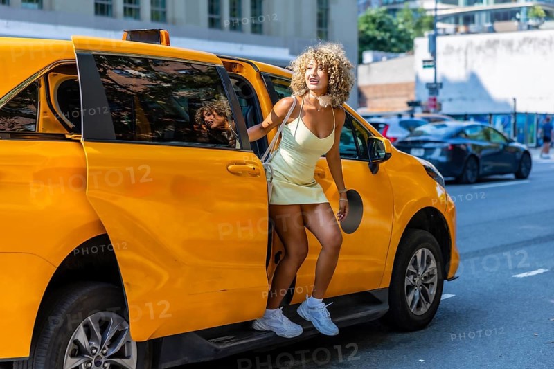 Young woman with curly hair stepping out of a classic yellow taxi on a vibrant new york city street, showcasing urban lifestyle and transportation