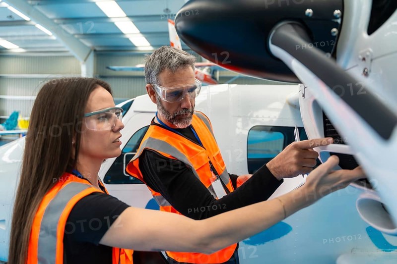 Two aerospace engineers wearing safety vests and goggles, carefully examining an airplane engine for maintenance and pre flight checks in an aircraft hangar