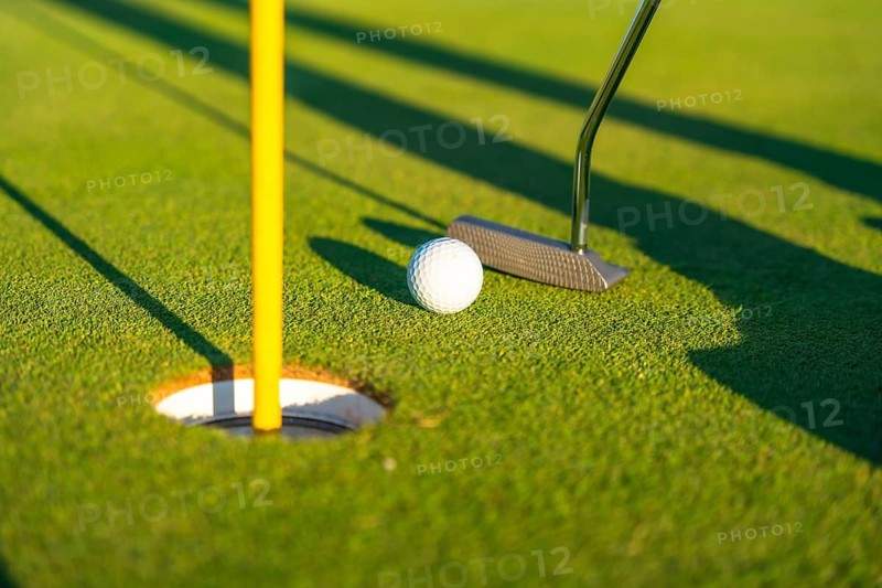 Close-up photo of a golf club, ball and hole in a green golf course