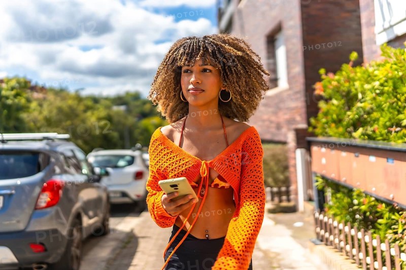 Latin young woman using phone walking next to houses in a residential district