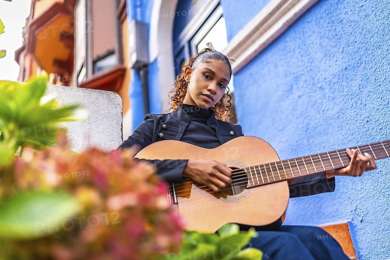 Low angle view photo of a beauty young african american woman playing the guitar next to colorful house in a city