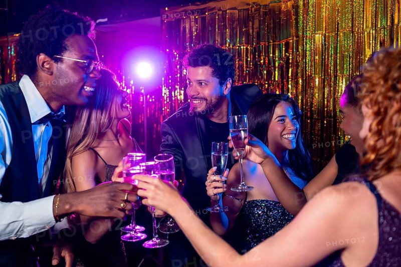 Cheerful elegant friends are toasting with champagne flutes, enjoying a glamorous party in a nightclub