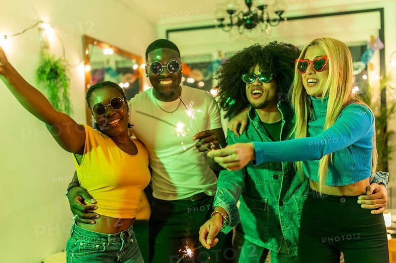Multi-ethnic friends dancing waving sparkles during home party together