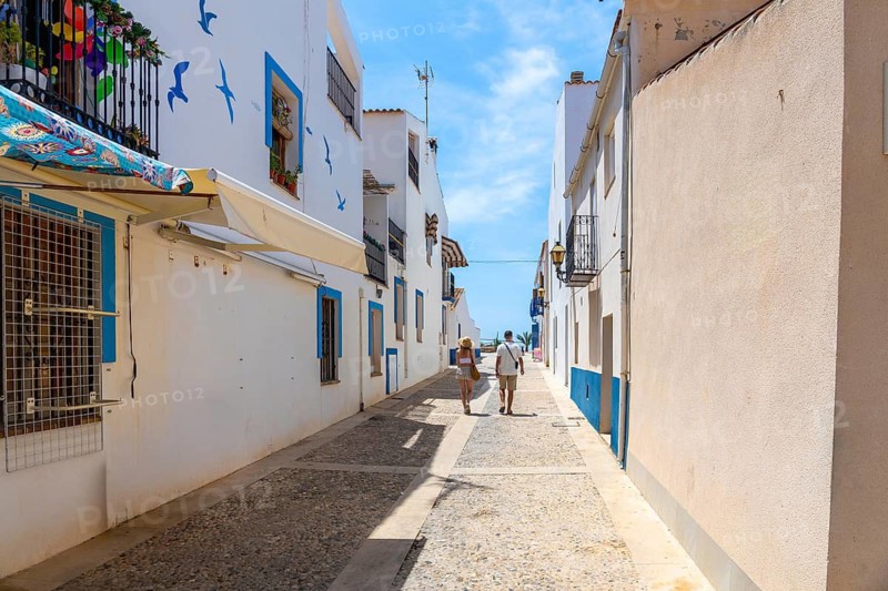 Couple enjoying summer vacation, walking along a charming narrow street of white houses with blue accents, leading towards the sea on tabarca island, alicante, spain
