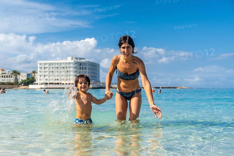 A woman and a child are playing in the ocean. The woman is holding the child's hand