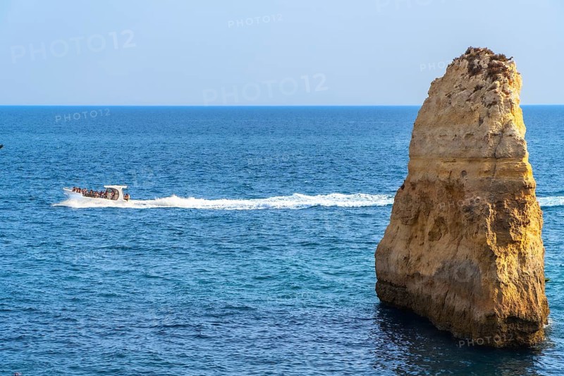 Motorboat full of tourists sailing near a majestic sea stack in the beautiful algarve region of portugal, offering breathtaking views of the coastline and crystal clear waters