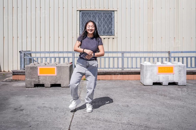 Frontal full length photo of a smiling young asian woman dancing K-pop in an industrial roof