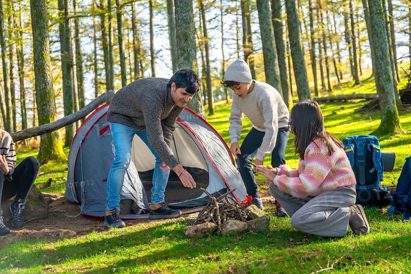 Caucasian family with three child preparing open fire on camping trip