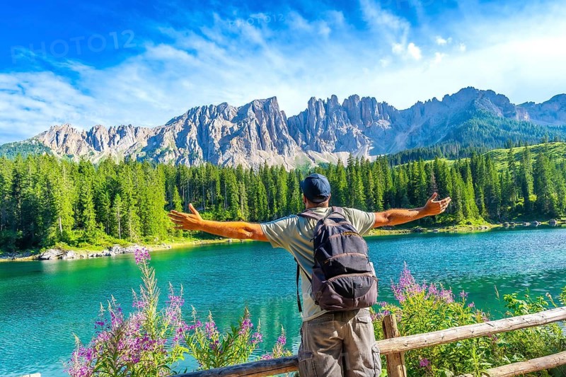 Hiker embracing the stunning panorama of lake carezza with the latemar mountain range in the background, dolomites, italy