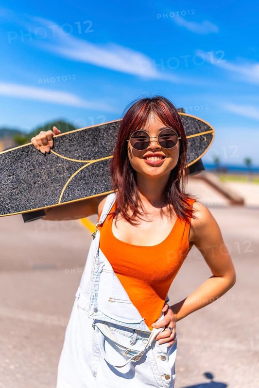 Vertical portrait of a young woman in summer clothes and sunglasses carrying skate on shoulders