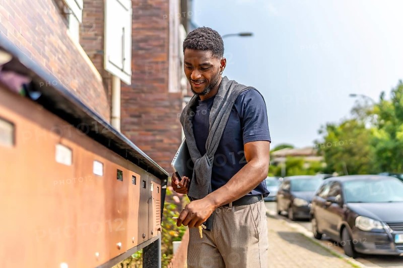 Young african businessman checking the mailbox on the street while carrying laptop