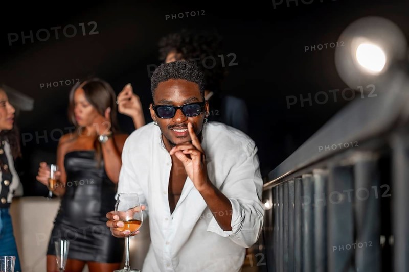 Latin cool man gesturing while dancing and drinking alcohol during roof party at night