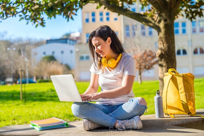 Concentrated student using laptop sitting on the grass of the campus