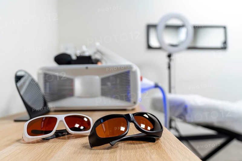 Protective glasses for patient and specialist placed on a wooden table, in an aesthetic medicine clinic with a laser machine preparing for a tattoo removal procedure or skin treatment