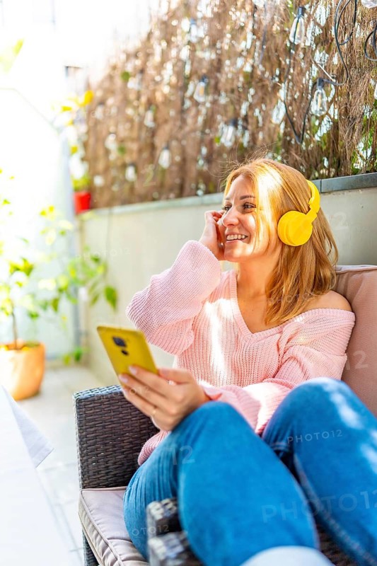 Vertical photo of a caucasian adult woman listening to music and using mobile phone in the courtyard