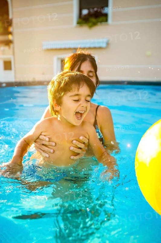 Happy mother teaching her son to swim in a pool during a sunny summer vacation, enjoying a playful moment together