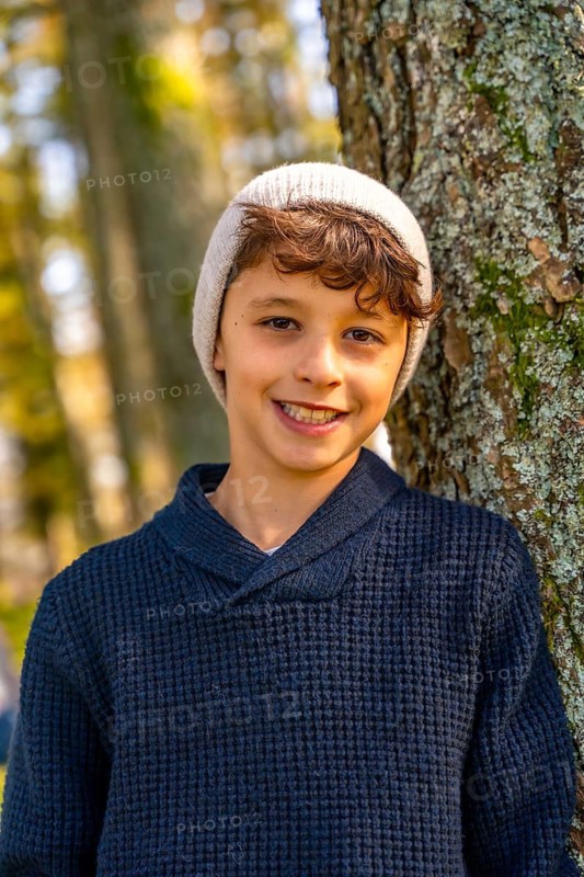 Vertical close-up portrait of a urban Teenager with hat leaning in a tree trunk smiling at camera in the forest