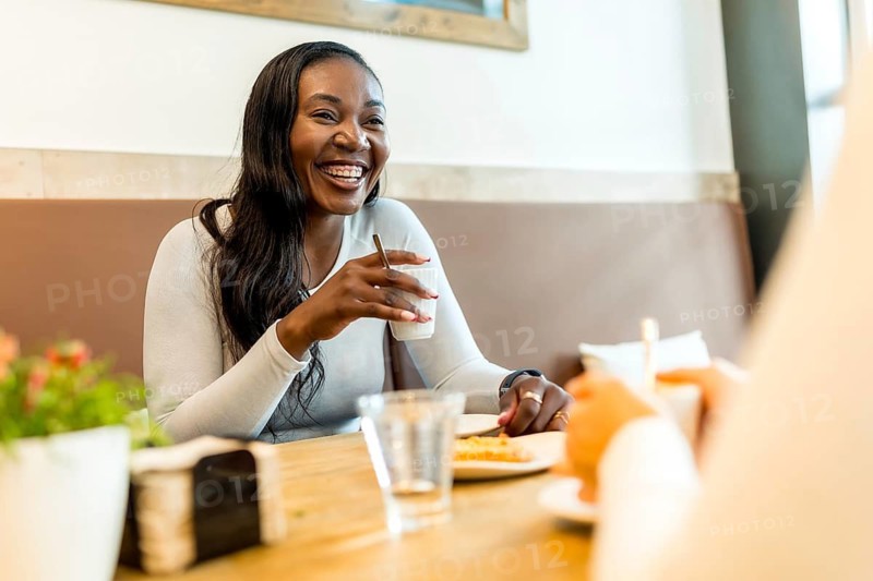 Cheerful black woman laughs during a coffee break with friends in a cozy cafe, savoring the moment and enjoying a pastry