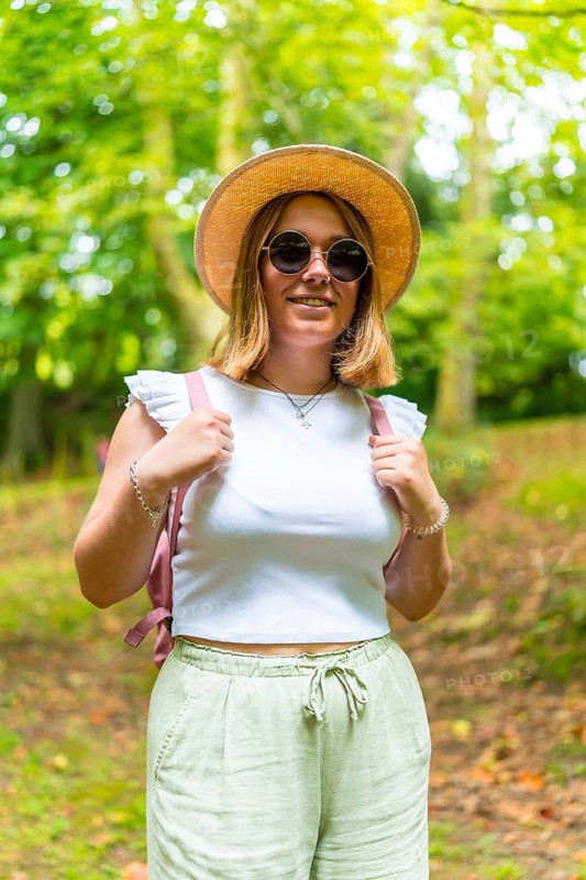 Vertical portrait of a caucasian young adult woman in summer clothes and sunglasses smiling while hiking in the forest