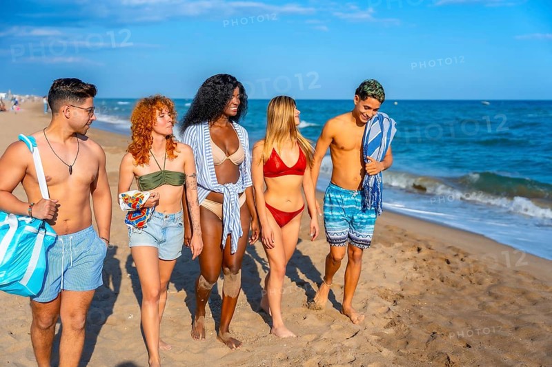 Multi ethnic group of friends walking along the beach, soaking up the sun and enjoying their summer vacation filled with laughter and joy